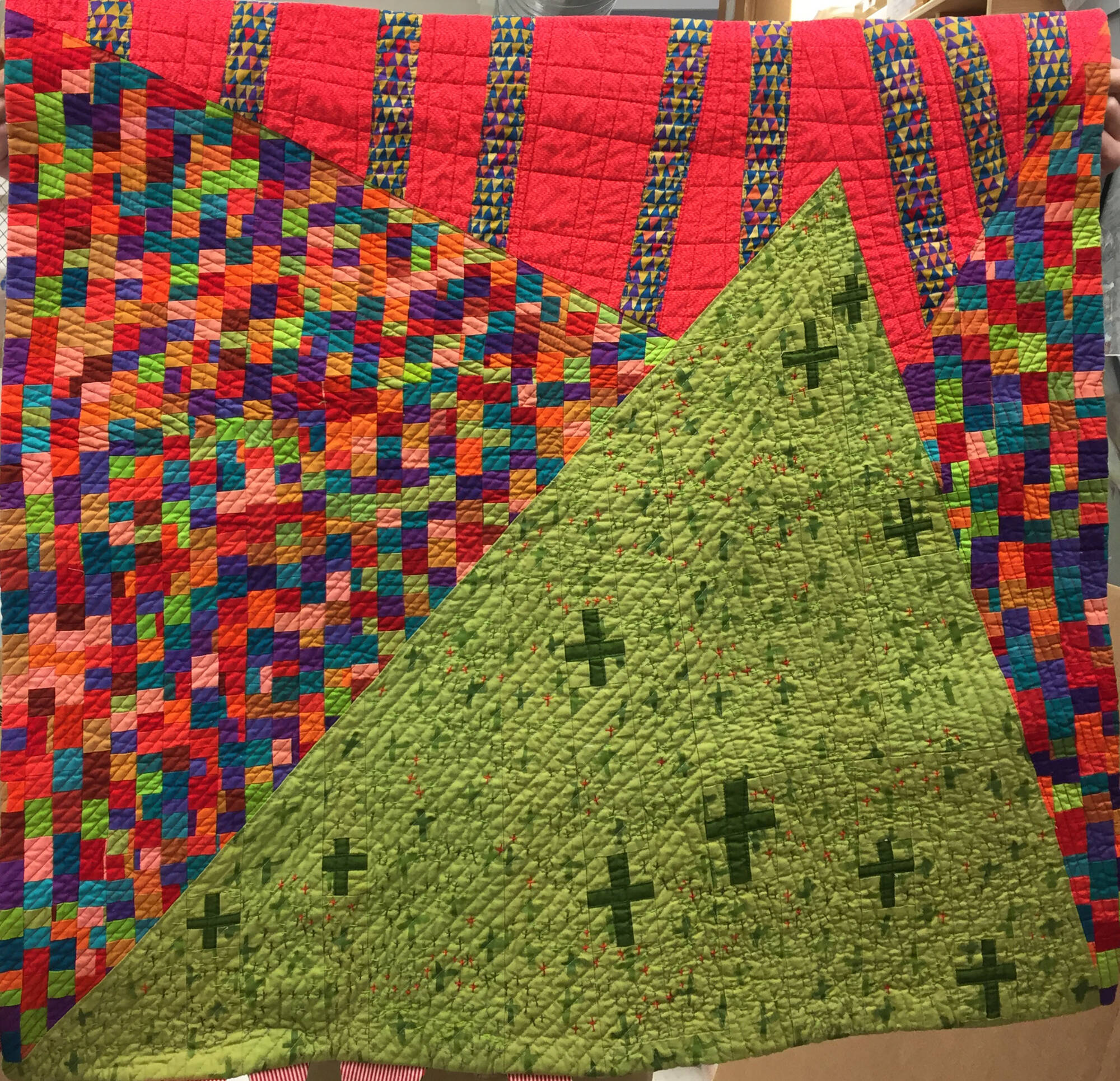 Geometric fabric quilt made of tiny squares of fabric. Large green trian with multi-colored squares behind it.